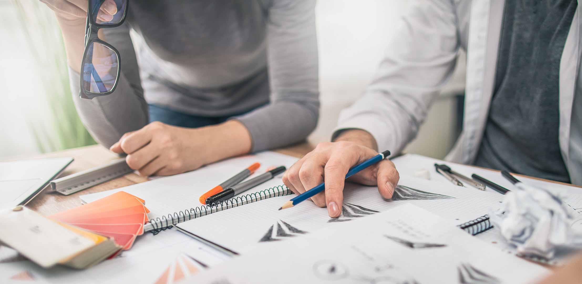 A photo of 2 people looking at logo concept sketches for a Brand Strategy on a desk.
